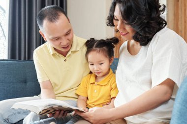 Gülümseyen Vietnamlı anne ve baba küçük kızına ilginç bir kitap gösteriyor.