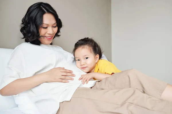 Feliz Niña Vietnamita Sonriente Abrazando Madre Embarazada Cuando Están Acostados — Foto de Stock