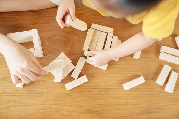 小さな娘が木造レンガの塔を建てるのを助ける母親の手 — ストック写真