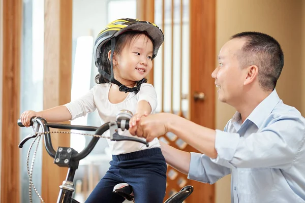 兴奋地微笑着的小女孩看着她的父亲解释如何骑自行车 — 图库照片