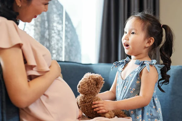 漂亮可爱的小女孩带着泰迪熊和她怀孕的妈妈谈论未来的兄弟姐妹 — 图库照片