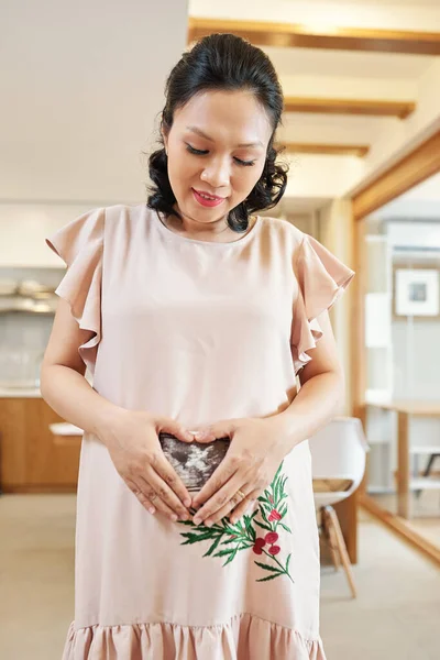 笑顔かわいいですアジアの女性でライトピンクドレス作るハートジェスチャーいつショー超音波スキャンの彼女の赤ちゃん — ストック写真