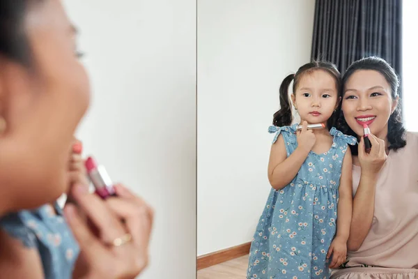 一个严肃的小女孩在家里重复着妈妈的话 在镜子前涂口红或唇膏 — 图库照片