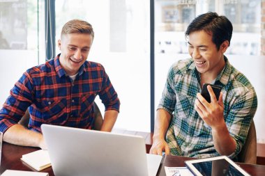 Mola sırasında laptoptan komik videolar izleyen neşeli çoklu etnik gençler.