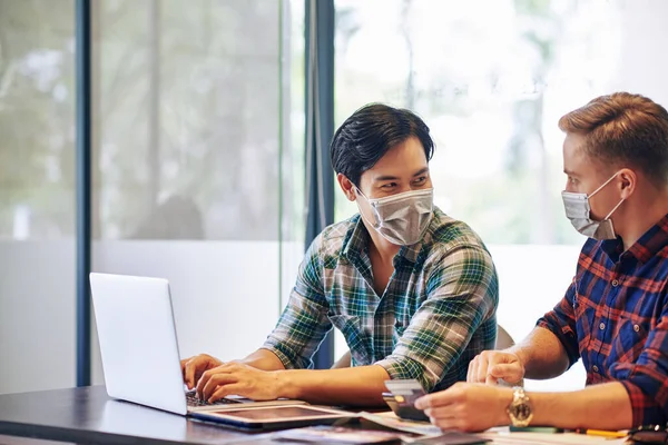 Positive Junge Menschen Medizinischen Masken Sitzen Bürotisch Und Diskutieren Über — Stockfoto