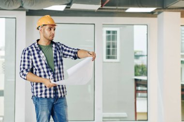 Bina binasının planlarını kontrol eden ciddi yakışıklı bir inşaat mühendisi.