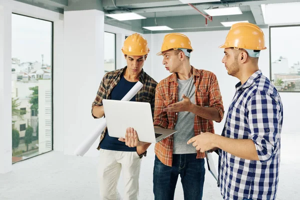 Equipe Jovens Engenheiros Sérios Chapéus Duros Discutindo Planta Construção Tela — Fotografia de Stock