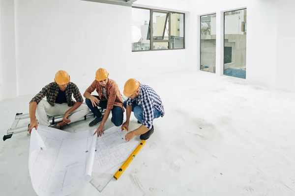 由戴硬帽的年轻建筑商组成的小组 在开始客户公寓翻新前 先核对蓝图 — 图库照片