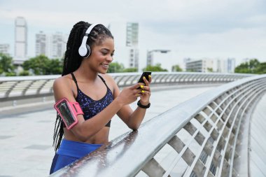 Köprüde duran ve akıllı telefondan koşusunu takip eden çekici, melez bir kadın.