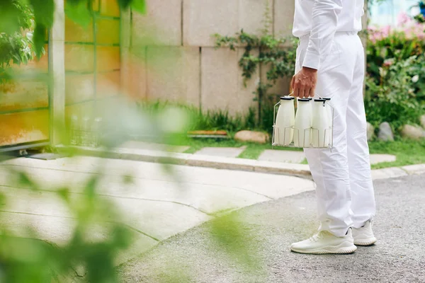 牛乳やヨーグルトのガラス瓶で家の入り口に立って白い制服を着たミルクマンの作物のイメージ — ストック写真