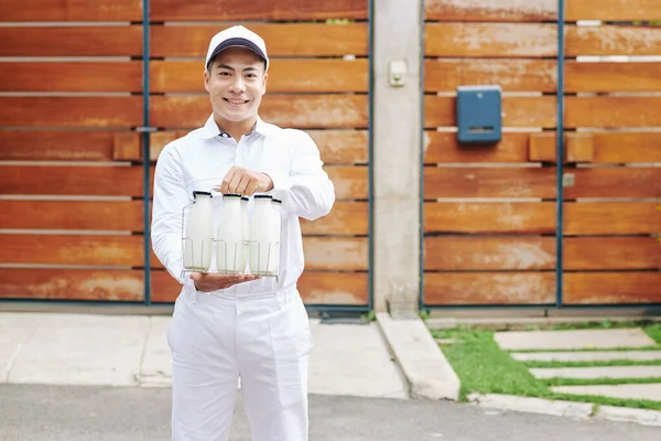 Happy young Asian milkman offering fresh milk in glass bottles