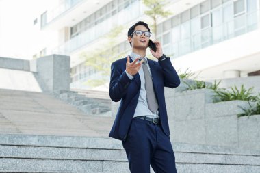 Genç Asyalı girişimci merdivenlerden inerken telefonla konuşuyor.