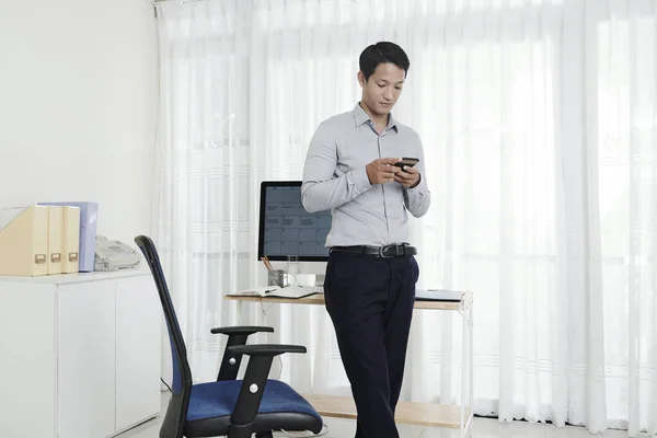 彼の家のオフィスに立って 彼の電話でテキストメッセージを読むベトナムのビジネスマン — ストック写真