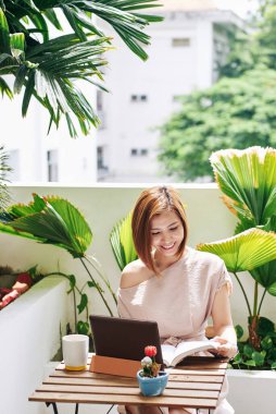 Kafe masasında kitap okuyan neşeli, güzel bir üniversite öğrencisi.