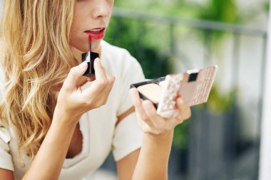 Kafede yemek yedikten sonra kırmızı sıvı ruj sürerken ayna kullanan genç bir kadın.