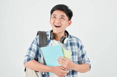 Şaşırmış Asyalı okul çocuğu elinde kitaplarla yukarı bakıyor ve heyecandan ağzını açıyor.