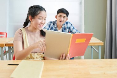 Gülümseyen Vietnamlı liseli kız arkadaşına sınav cevaplarını defterde gösteriyor.