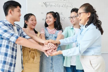 Bir grup öğrenci ve matematik öğretmeni matematik yarışmasından önce birbirlerine destek olmak için el ele tutuşuyorlar.