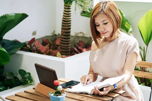 Güzel gülümseyen Asyalı kadın kafe masasında ilginç bir kitap okuyor.