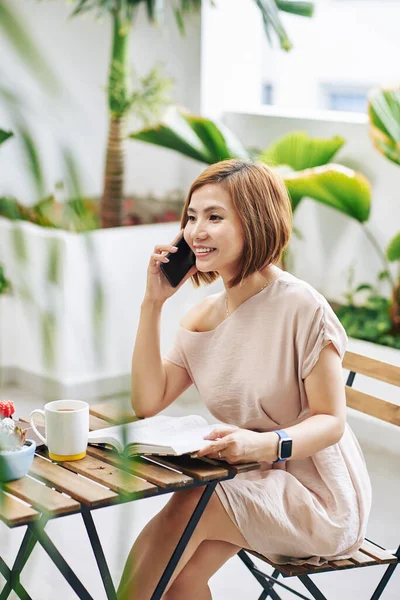 Joven Vietnamita Alegre Sentada Mesa Cafetería Con Libro Abierto Hablando —  Fotos de Stock