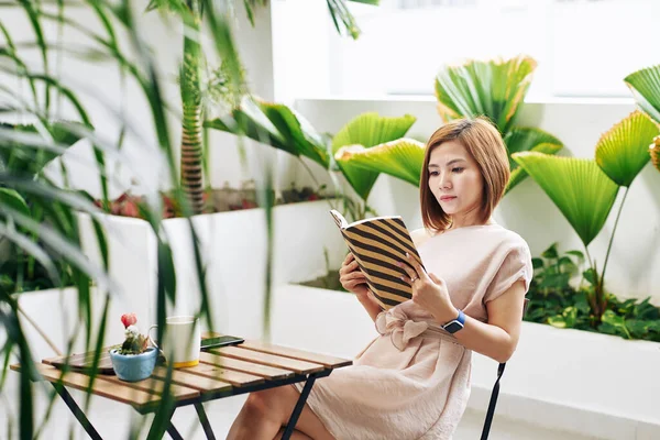 Серьёзная Молодая Азиатка Читает Увлекательную Книгу Столиком Кафе — стоковое фото