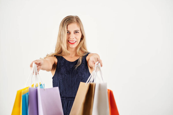 Cheerful young woman outstretching hands with shopping bags, isolated on white