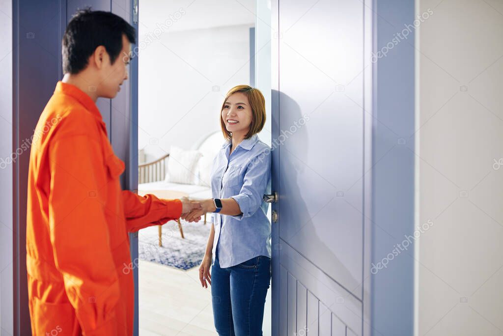 Smiling pretty housewife shaking hand of handyman in bright orange suit