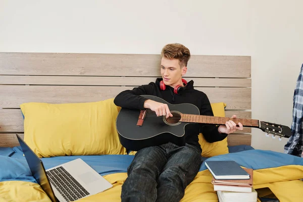聪明的少年在他的笔记本电脑上在线观看课 并学习如何弹吉他 — 图库照片