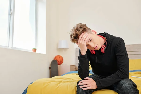 十代の男の子苦しみから重度の頭痛座っている彼のベッドの端 — ストック写真
