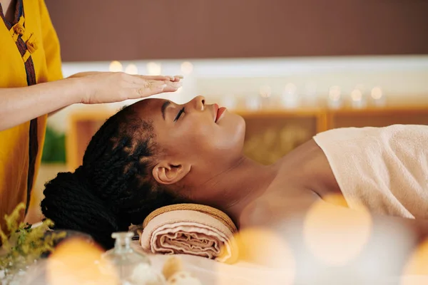 治療中にエネルギーを転送するためにかなり若い黒の女性の頭の上に手を握っているセラピストReikiセッション — ストック写真