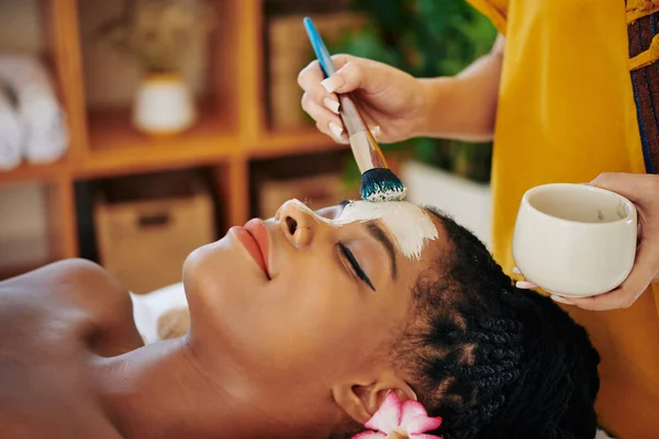 美容师在年轻貌美的黑人妇女脸上应用净化和减少毛孔的特写图像 — 图库照片