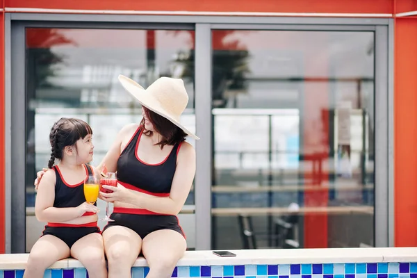 抱着母亲和女儿坐在游泳池边 喝着新鲜的水果鸡尾酒 — 图库照片