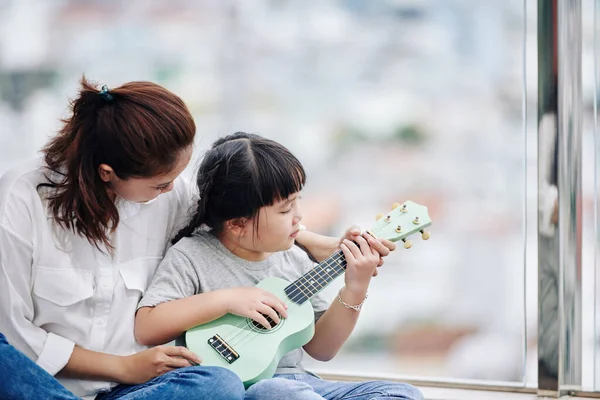Anne küçük kızına gitar çalmayı ve akorlarını göstermeyi öğretiyor.