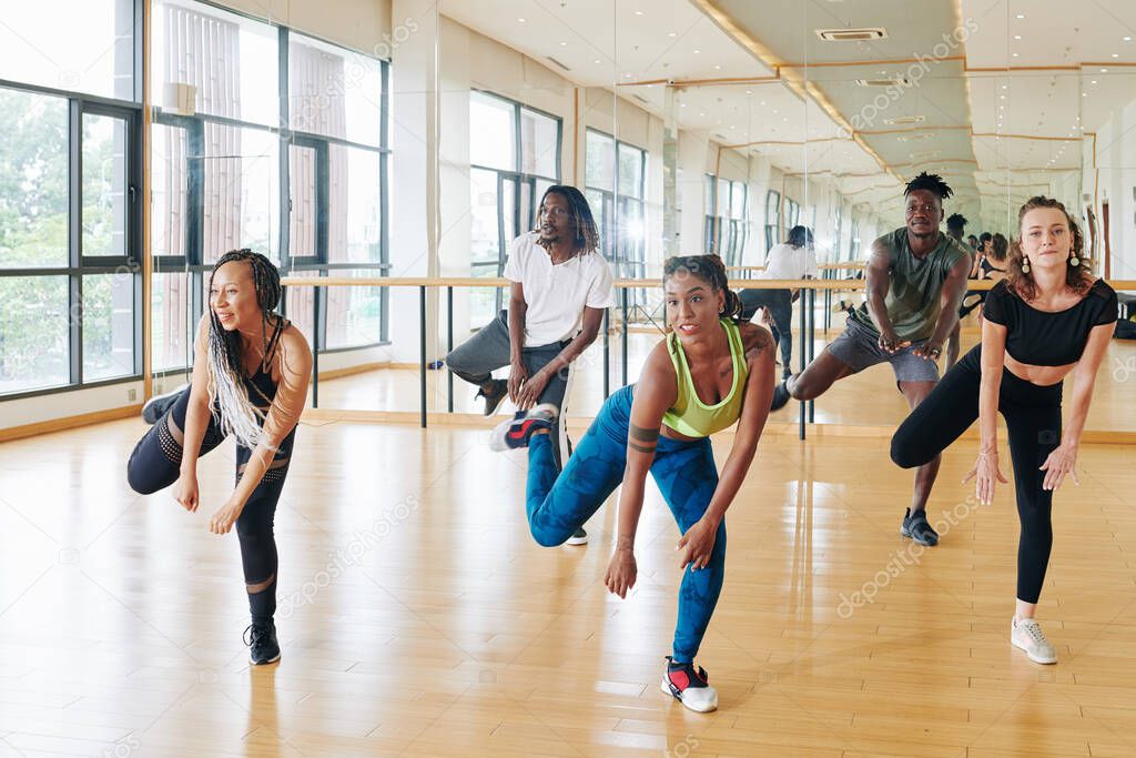 Pretty active young woman showing new movement to young people in dance class