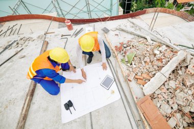 İnşaat mühendisleri bina planına işaret ediyor ve ayrıntıları tartışıyor, yukarıdan bakıyorlar