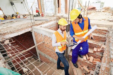 Ciddi inşaatçılar tuğla merdivenlerden çıkıp bugünkü iş planlarını tartışıyorlar.