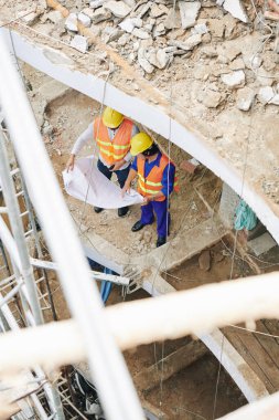 İnşaat halindeki binanın zemininde duran ve planların ayrıntılarını tartışan yapıcılar, yukarıdan görünüm
