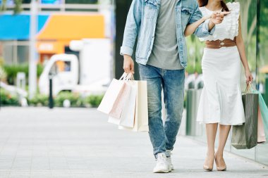 Alışveriş torbalarıyla sokakta yürüyen genç bir çiftin kesilmiş görüntüsü.