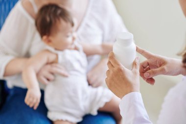 Çocuk doktorunun, küçük bir kızın annesine her gün hangi ilacı vermesi gerektiğini söylerken yakın plan görüntüsü.