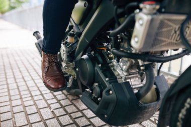 Deri ayakkabılı motosikletlinin pedala basma görüntüsü.