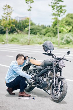 Hüsrana uğramış motosikletçi yolda bozuk bisikletini tamir ediyor.