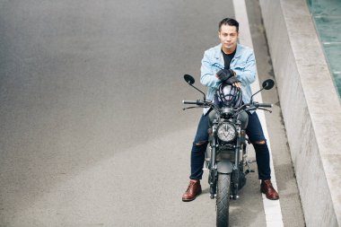 Ciddi derecede çekici Vietnamlı motorcu kaskını çıkarıyor ve yolda motosiklet üzerinde otururken kameraya bakıyor.