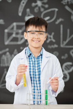 Gözlüklü neşeli Asyalı çocuğun portresi sınıfta kimyasal reaktörleri karıştırıyor.