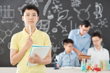 Matematik kitabı ve fen dersinde kimya denklemleri çözen düşünceli Vietnamlı öğrenci.