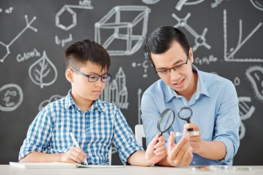 Kimya öğretmeni ve okul öğrencisi büyüteçle petri kabının içine bakıyor.