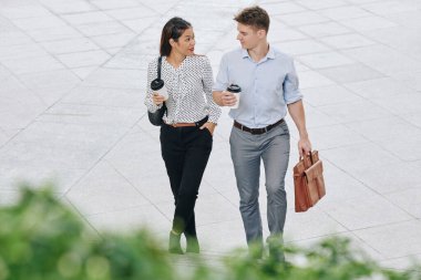 İş ortaklarının elinde kahve tutarak kağıt bardaklara girip sokakta yürüdükleri yüksek açılı bir manzara.