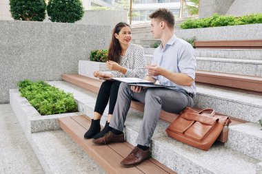 Genç finans yöneticileri açık havada oturup raporları, çizelgeleri ve grafikleri tartışıyor.