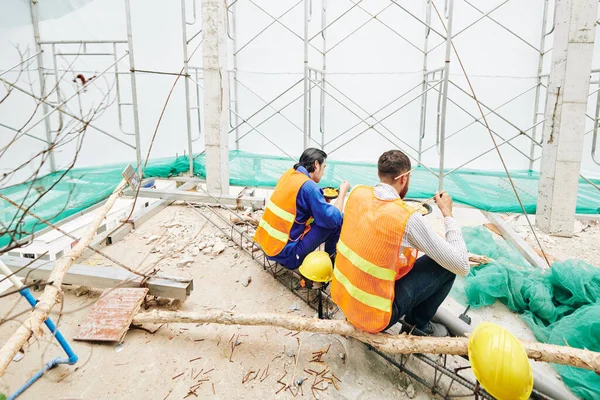 身穿橙色背心的建筑商坐在正在施工的大楼房间里享用美味的拉面午餐 从后面看 — 图库照片