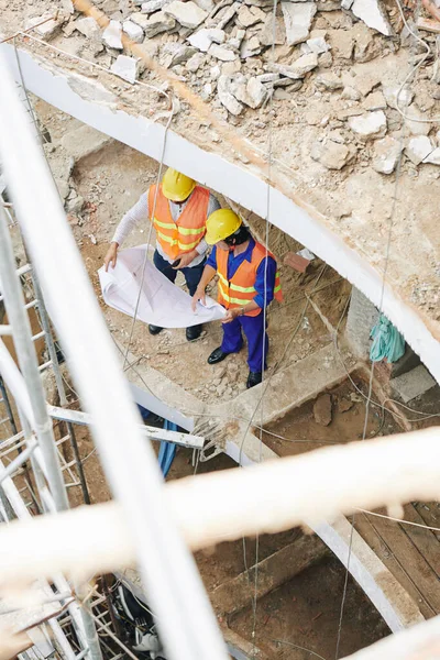 İnşaat halindeki binanın zemininde duran ve planların ayrıntılarını tartışan yapıcılar, yukarıdan görünüm