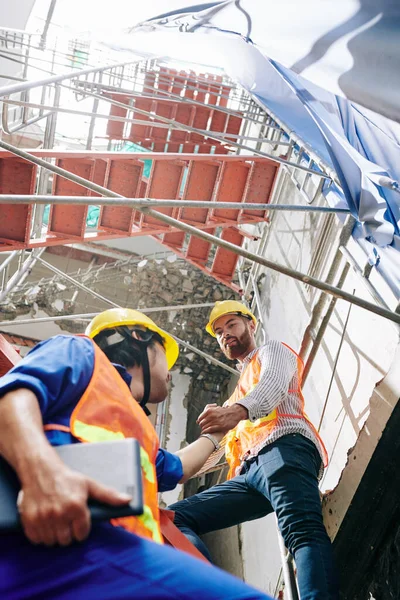 Stavitel Vestě Klobouku Pomáhá Kolegovi Vylézt Lešení Před Budovou Výstavbě — Stock fotografie